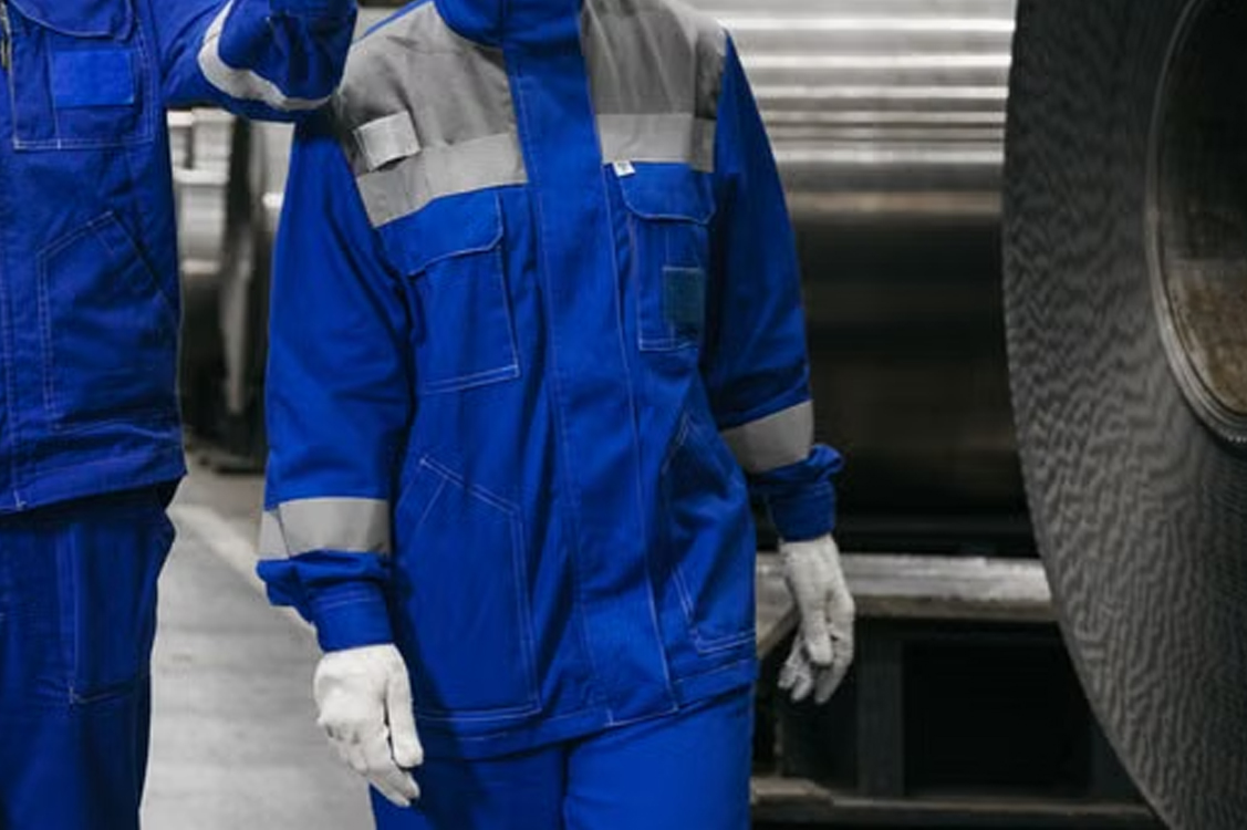 Workers in protective clothing beside steel coils in a factory